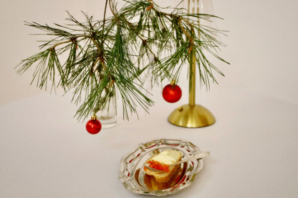 Pine branch with red ornaments and appetizer on elegant table setting, perfect for holiday themes.
