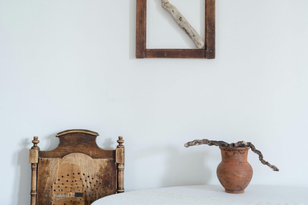 A minimalist rustic setting featuring a wooden chair, clay pot, and driftwood art on a white wall.