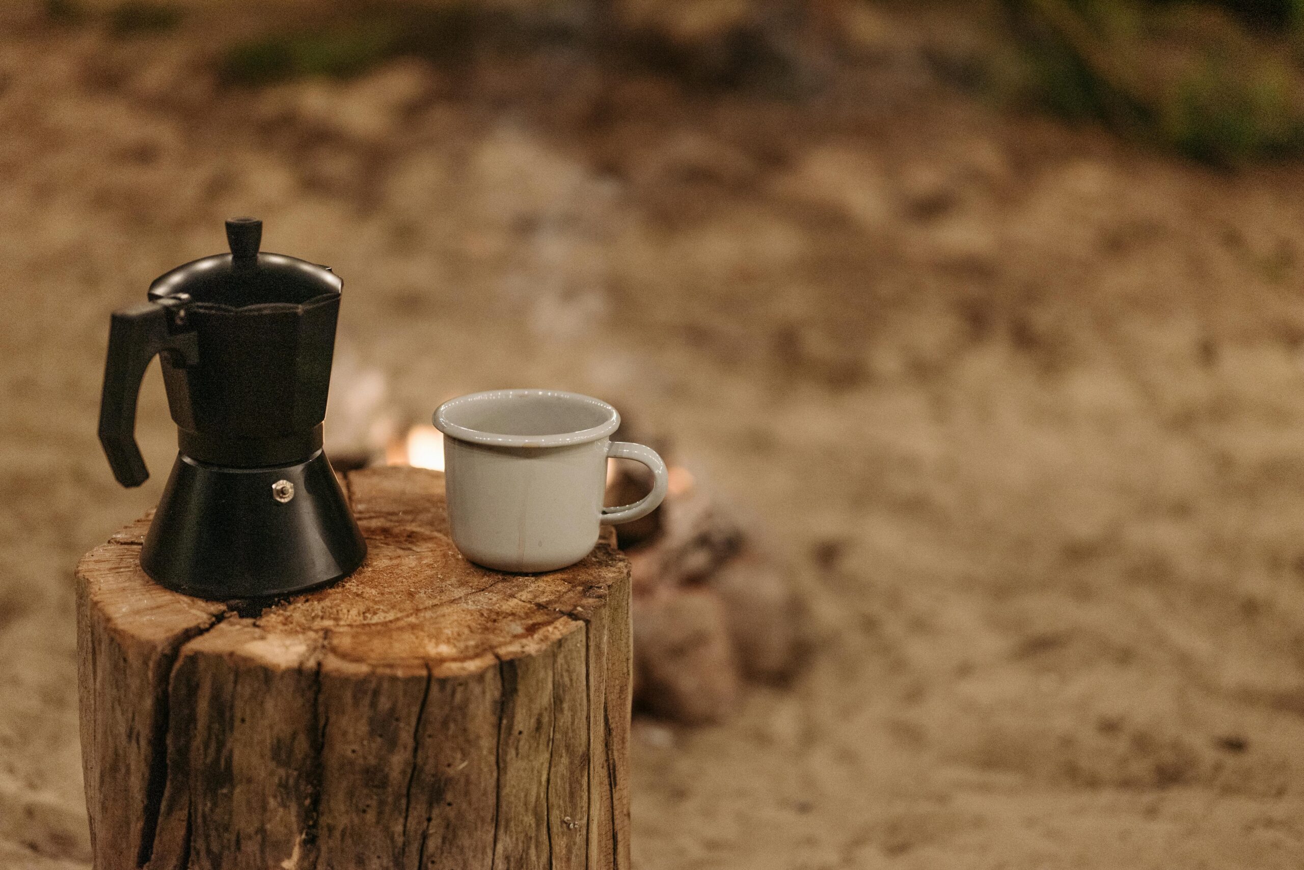 A moka pot and ceramic cup placed on a tree stump outdoors, perfect for a cozy coffee moment.