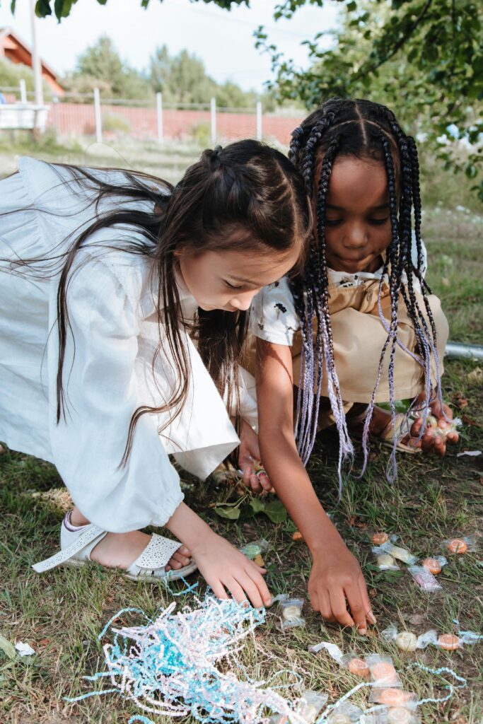 Two children picking up candy from the grass at an outdoor party.
