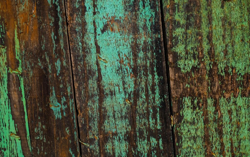 Detailed view of an aged wooden surface with peeling green paint, showcasing texture and decay.