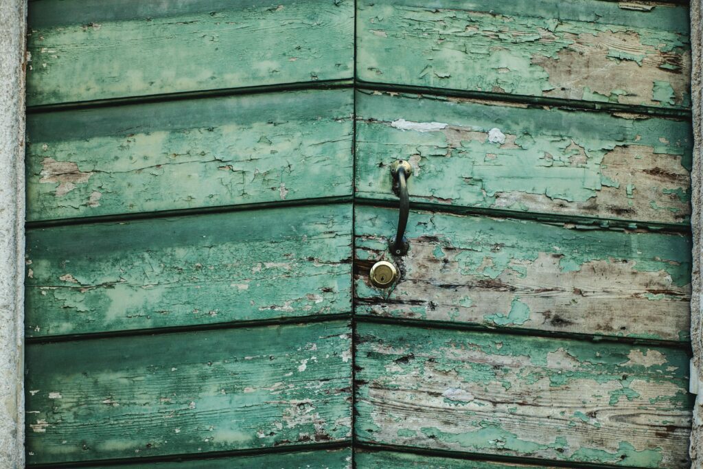 Close-up of a weathered green wooden door with peeling paint in Vicenza, Italy.